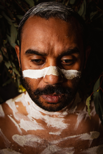 Painted up Aboriginal male headshot with leaves in background - Australian Stock Image