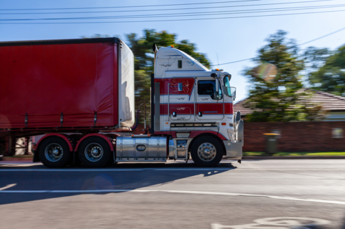 Panning shot of truck traveling along highway through town with motion blurred background - Australian Stock Image