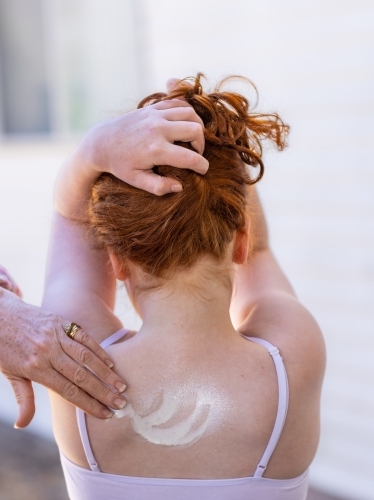 parent's hand applying sunscreen to her pale daughter's back - Australian Stock Image