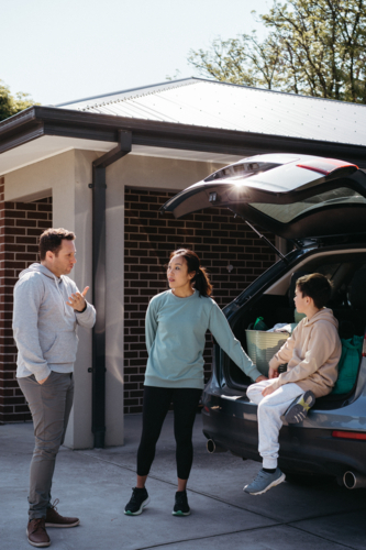Parents having a conversation while young boy sits on the car with boot open - Australian Stock Image