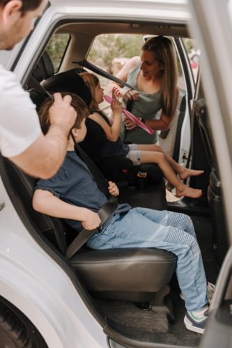 Parents securing their children in the car seat with a belt. - Australian Stock Image