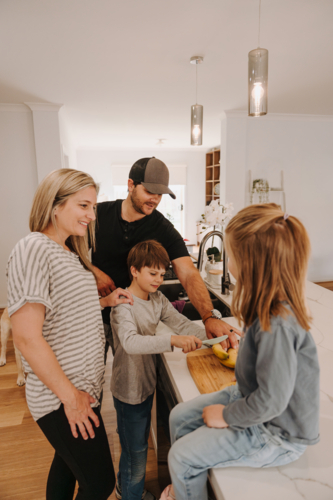 Parents teaching kids how to cut fruits in the kitchen. - Australian Stock Image