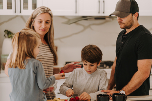 Parents teaching kids how to cut fruits in the kitchen. - Australian Stock Image