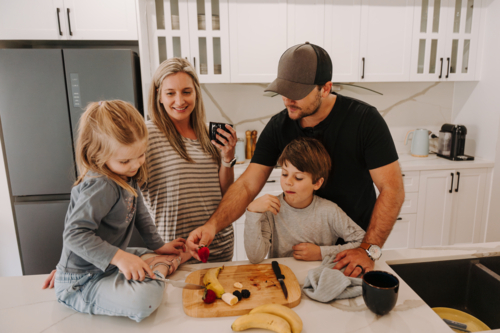 Parents teaching kids how to cut fruits in the kitchen. - Australian Stock Image