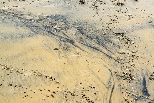 Patterns in wet yellow and black mineral sands on a beach at low tide - Australian Stock Image