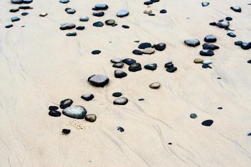 Patterns in wet yellow and black mineral sands on a beach at low tide with pebbles - Australian Stock Image