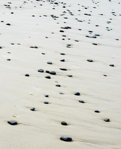 Patterns in wet yellow and black mineral sands on a beach at low tide with pebbles - Australian Stock Image