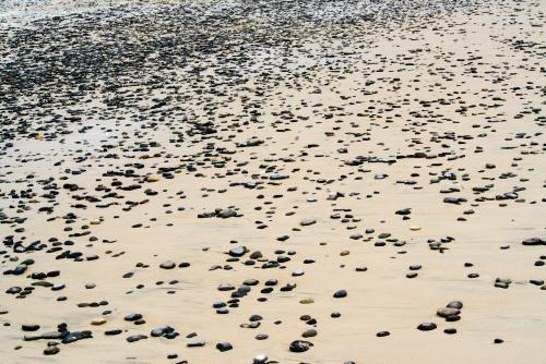 Pebbles scattered on a sand beach at low tide with foam - Australian Stock Image