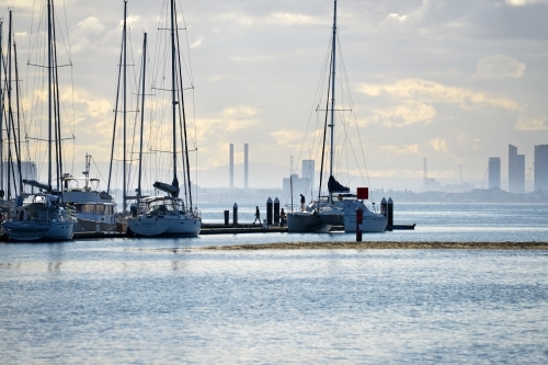 People disembark a yacht at Middle Brighton Pier with the city skyline in the background - Australian Stock Image