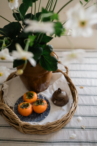 persimmons on a vintage woven tray with Japanese windflowers - Australian Stock Image