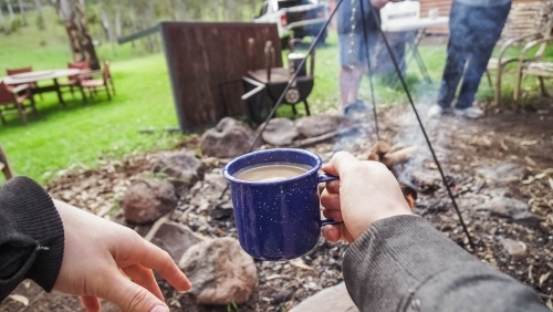 Person holding coffee cup over campfire - Australian Stock Image