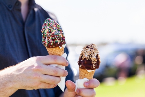 Person holding out soft serve ice cream with chocolate topping and sprinkles on summers day - Australian Stock Image