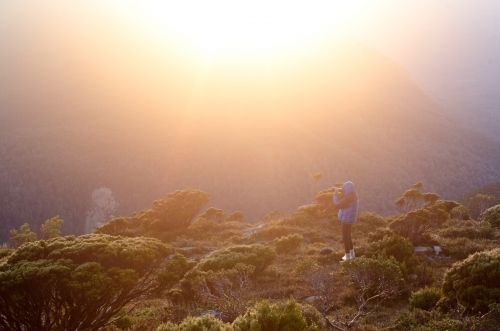 Person looking through binoculars at mountain range at sunset