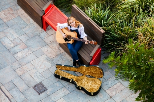 Person playing guitar on street footpath busking - Australian Stock Image