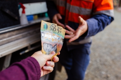 Persons hand passing over money for cash payment to handyman - paying in cash - Australian Stock Image