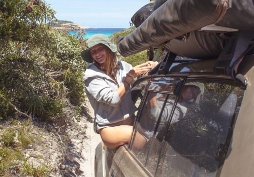 Photo of smiling woman hanging out the window of a 4wd car on a track headed to the blue ocean - Australian Stock Image