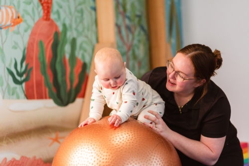 physiotherapist with baby on physio ball doing vestibular stimulation rocking gently - Australian Stock Image