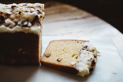 Piece of sliced almond cake on rustic wooden table and marble platter - Australian Stock Image