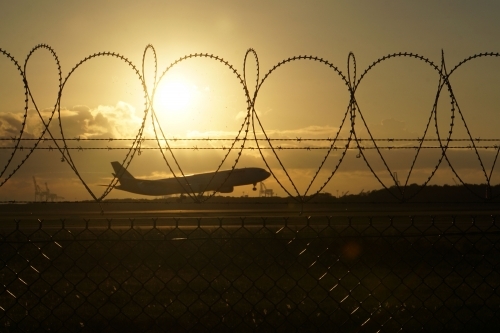 Plane landing at sunrise through security fence - Australian Stock Image