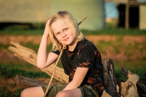 Portrait image of farm boy with long blonde hair holding stick - Australian Stock Image