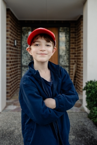 Portrait of a happy, young Australian boy wearing a red cap standing outside his home - Australian Stock Image