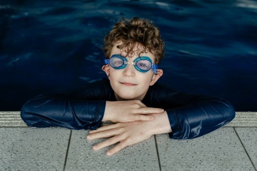 Portrait of a happy young boy wearing swimming goggles learning to swim in an indoor swimming pool - Australian Stock Image