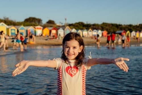 Happy, young girl with arms outstretched in front of the beach bathing boxes (huts), Brighton Beach - Australian Stock Image