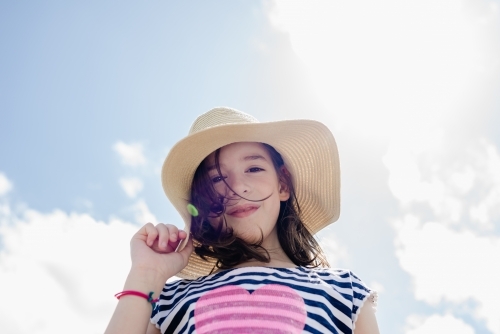 Portrait of a happy, young girl wearing a sun hat against a blue sky - Australian Stock Image