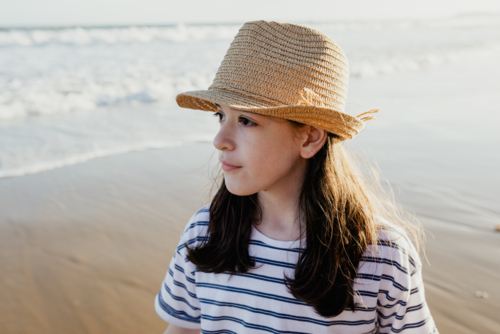 Portrait of a happy young girl wearing a sunhat at the beach in the afternoon - Australian Stock Image