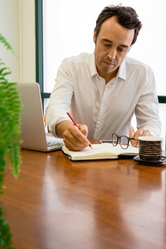 Portrait of a male office worker sitting with laptop and note book at a meeting table - Australian Stock Image