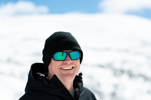 Portrait of a man looking down dressed in warm black outdoor coat and cap with blurred snow-covered - Australian Stock Image