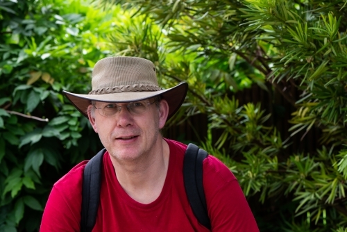 Portrait of a mature male tourist wearing an Australian hat and a backpack with greenery behind