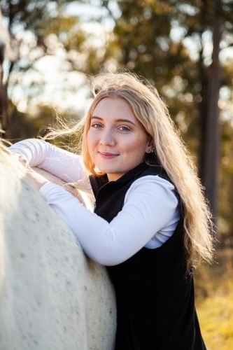 Portrait of a smiling blonde teen resting on her horse - Australian Stock Image