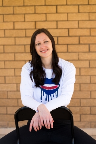 Portrait of a smiling woman with long dark hair, sitting astride a chair - Australian Stock Image