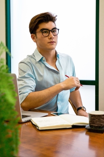 Portrait of a young male office worker sitting with laptop and note book at a meeting table