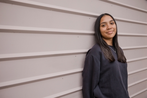 Portrait of a young, smiling,  first nations woman against wall outside - Australian Stock Image
