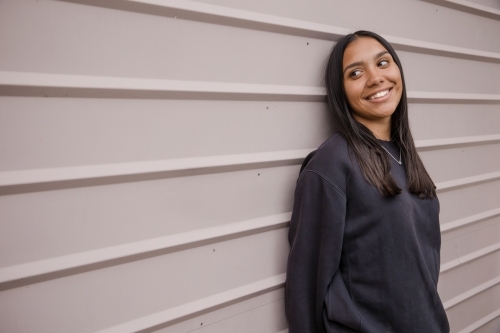 Portrait of a young, smiling,  first nations woman against wall outside - Australian Stock Image