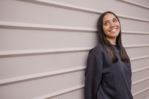 Portrait of a young, smiling,  first nations woman against wall outside - Australian Stock Image