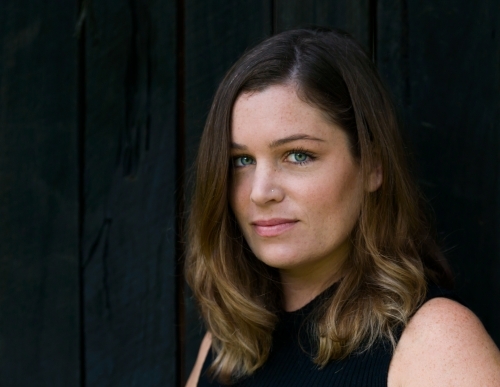 Portrait of a young woman with long brown hair, blue eyes and dark background - Australian Stock Image