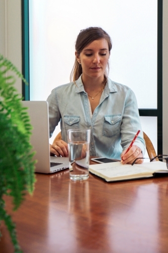 Portrait of an office worker sitting with laptop and note book at a meeting table - Australian Stock Image