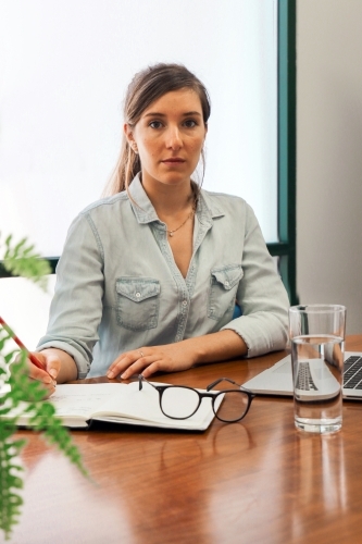Portrait of an office worker sitting with laptop and note book at a meeting table - Australian Stock Image