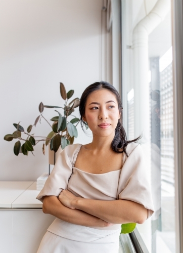 Asian woman standing by the window in an office - Australian Stock Image