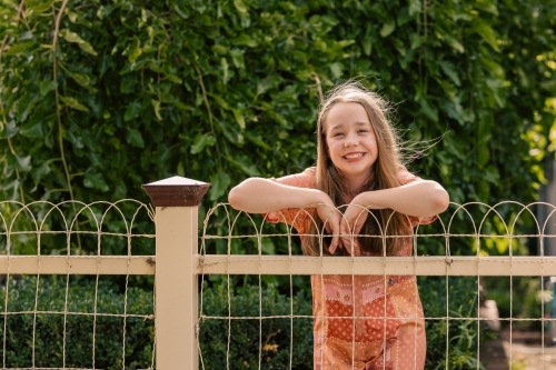 Portrait of cheerful pre-teen girl leaning on wire fence in country town - Australian Stock Image