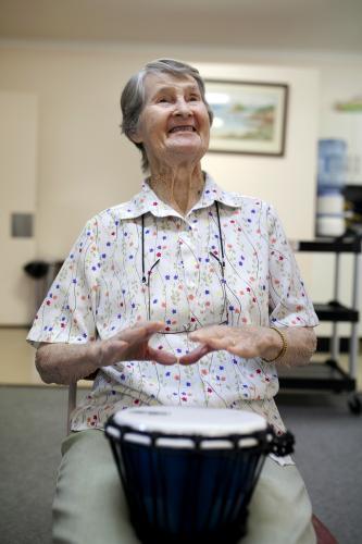 Portrait of happy elderly lady during bongo drumming session at retirement village - Australian Stock Image