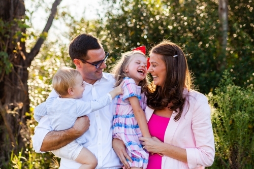 Portrait of happy family of four with a girl and boy child and parents laughing together outside - Australian Stock Image