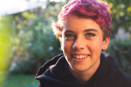 Portrait of happy, smiling teenage girl with short hair in vibrant, natural outdoor setting - Australian Stock Image