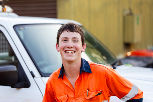 Portrait of happy smiling young male trade apprentice in high-vis workwear beside ute vehicle - Australian Stock Image