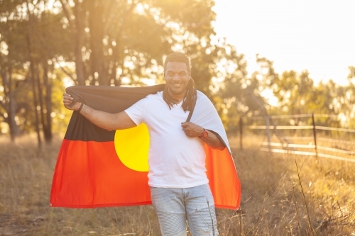 Portrait of smiling first nation australian man holding aboriginal flag in paddock - Australian Stock Image