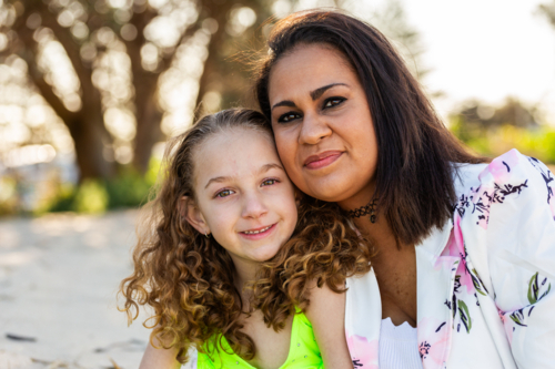 Portrait of Torres Strait Islander mother in her thirties and young daughter together on the beach - Australian Stock Image