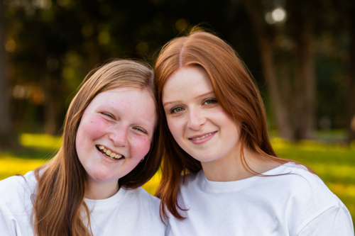 Portrait of twin seventeen year old redhead girls with heads together outdoors - Australian Stock Image